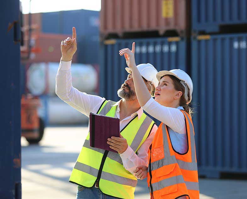 Two workers in hi-vis vests checking container stacks in a port yard